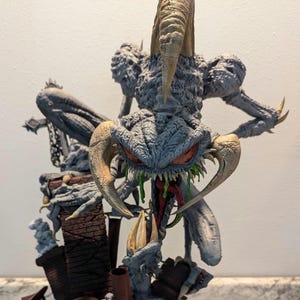 May include: A detailed, gray and green painted figurine of a demonic creature with sharp teeth and horns. The creature is posed in a menacing stance, with its claws extended and its mouth open in a snarl. The figurine is set against a backdrop of a brick chimney and smoke.
