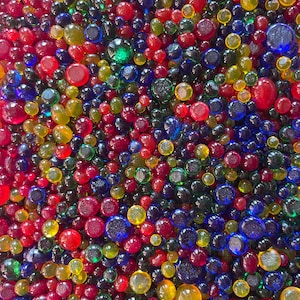 May include: A close-up image of a large collection of colorful glass beads. The beads are various shades of red, blue, green, and yellow. The beads are all round and have a smooth, glossy finish.