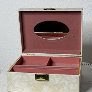 May include: A white jewelry box with a gold latch and a pink velvet interior. The box has a small oval mirror inside the lid.