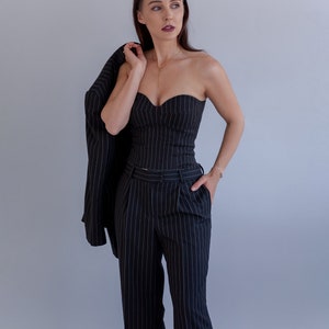 Pode incluir: Uma mulher vestindo um terno de riscas finas preto e branco. O terno inclui um top sem al&ccedil;as e cal&ccedil;as. A mulher est&aacute; segurando um blazer sobre o ombro.