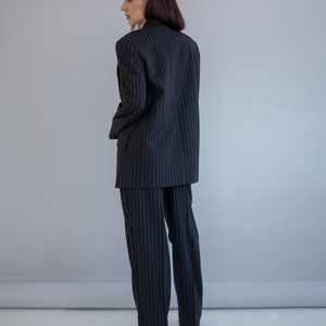 Pode incluir: Um fato de riscas finas preto e branco com blazer e cal&ccedil;as.