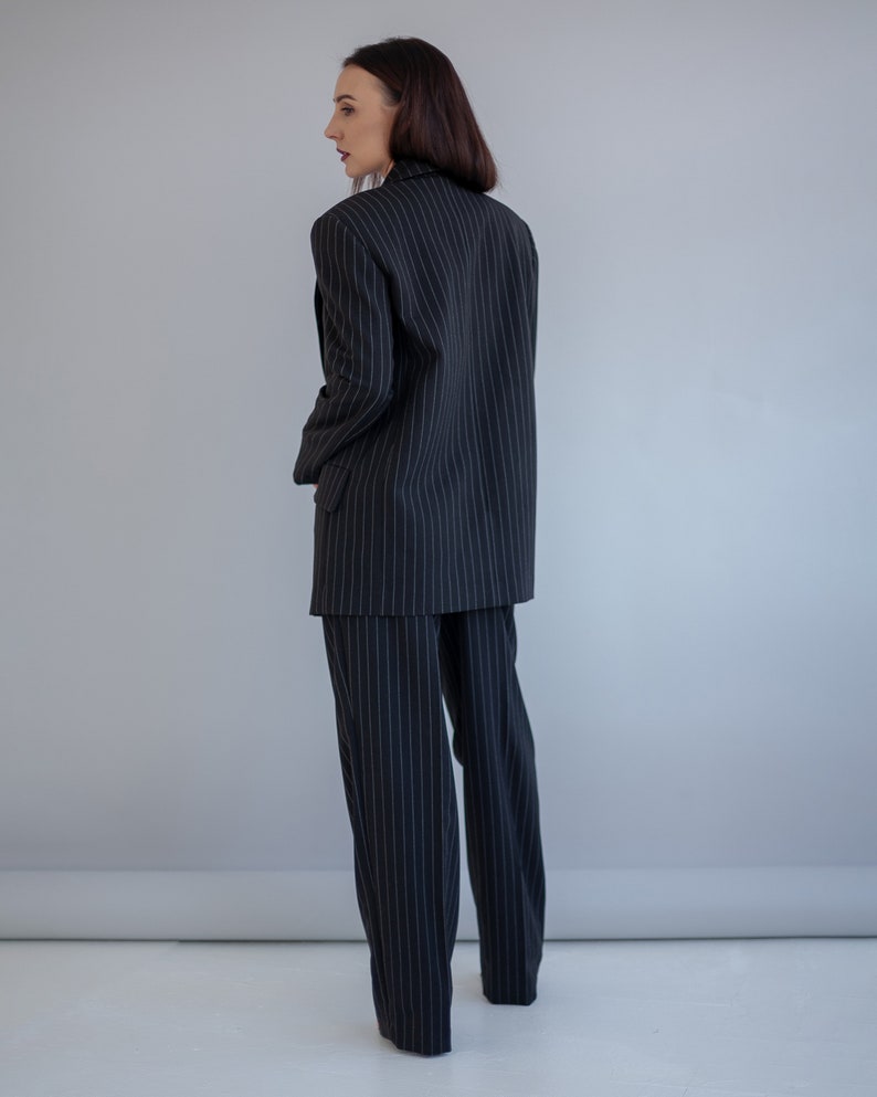 Pode incluir: Um fato de riscas finas preto e branco com blazer e cal&ccedil;as.
