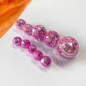 Puede incluir: Un conjunto de nueve bolas de discoteca esf&eacute;ricas de distintos tama&ntilde;os, cubiertas con peque&ntilde;os espejos cuadrados de color rosa reflectante. Las esferas est&aacute;n dispuestas en dos filas y presentan un acabado rosa met&aacute;lico brillante.