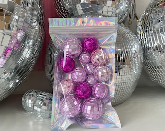 May include: A clear, iridescent resealable plastic bag filled with a collection of small, spherical disco balls in various shades of pink and magenta. Each ball is covered in tiny, reflective square mirror tiles that catch and reflect light.
