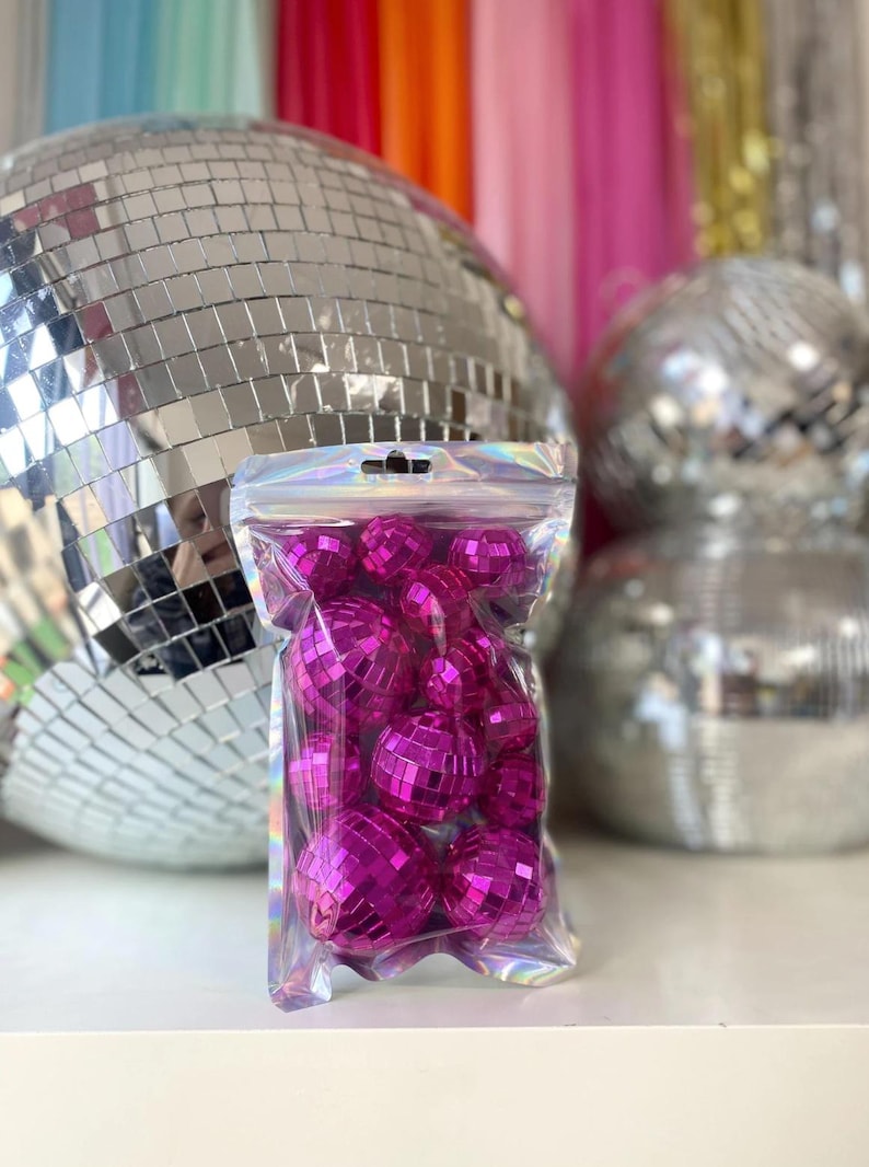 Puede incluir: Una bolsa de pl&aacute;stico transparente, iridiscente y resellable llena de m&uacute;ltiples bolas de discoteca peque&ntilde;as y redondas de color rosa intenso. Cada bola de discoteca en miniatura est&aacute; cubierta con diminutos espejos cuadrados.