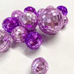 Puede incluir: Una colecci&oacute;n de bolas de discoteca esf&eacute;ricas en varios tonos de morado y rosa claro. Cada bola est&aacute; cubierta con peque&ntilde;os azulejos de espejo cuadrados y reflectantes que crean una superficie facetada. Las esferas var&iacute;an en tama&ntilde;o y grupo.