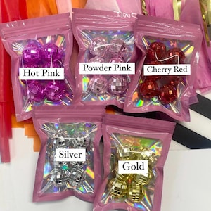 Pode incluir: Cinco pequenas bolsas sel&aacute;veis contendo ornamentos de bola de discoteca reflexivos em rosa choque, rosa p&oacute;, vermelho cereja, prata e ouro. Cada bolsa possui uma janela transparente e uma etiqueta branca identificando a cor dos objetos esf&eacute;ricos.