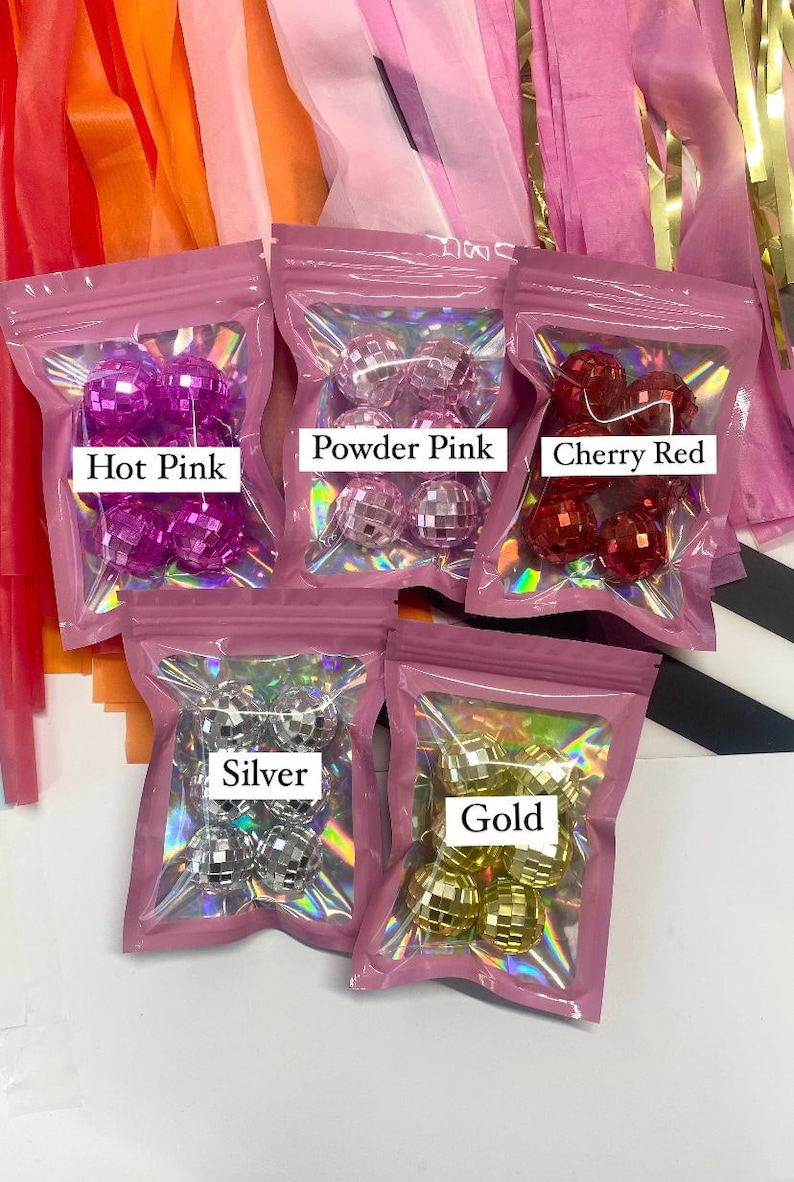 Pode incluir: Cinco pequenas bolsas sel&aacute;veis contendo ornamentos de bola de discoteca reflexivos em rosa choque, rosa p&oacute;, vermelho cereja, prata e ouro. Cada bolsa possui uma janela transparente e uma etiqueta branca identificando a cor dos objetos esf&eacute;ricos.