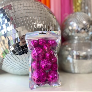 Pode incluir: Um saco de pl&aacute;stico transparente e iridescente com fecho, contendo uma cole&ccedil;&atilde;o de pequenas bolas de discoteca redondas em cor-de-rosa choque. Cada bola est&aacute; coberta por min&uacute;sculos espelhos quadrados refletores que captam a luz.