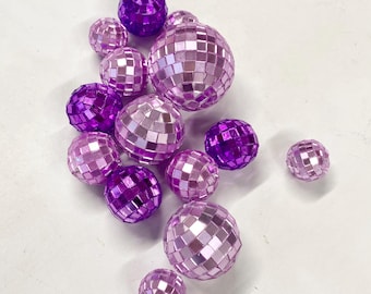 May include: A collection of spherical disco balls in various sizes, featuring a reflective mosaic surface made of small square mirrors. The spheres are colored in shades of deep purple, light lavender, and soft pink, creating a gradient effect.