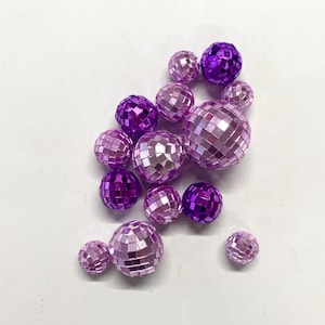 Puede incluir: Una colecci&oacute;n de bolas de discoteca esf&eacute;ricas de varios tama&ntilde;os, con una superficie reflectante compuesta por peque&ntilde;os azulejos de espejo cuadrados de color p&uacute;rpura y rosa claro. El conjunto incluye m&uacute;ltiples esferas de diferentes di&aacute;metros, todas con un acabado met&aacute;lico que capta la luz en sus superficies facetadas.