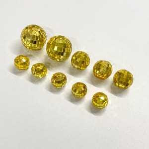Puede incluir: Un conjunto de diez bolas de discoteca esf&eacute;ricas de distintos tama&ntilde;os, cubiertas con peque&ntilde;os espejos cuadrados dorados y reflectantes. Las esferas est&aacute;n dispuestas en un grupo suelto, mostrando el acabado dorado met&aacute;lico y el patr&oacute;n de cuadr&iacute;cula.