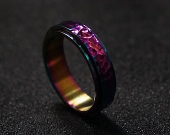 May include: A hammered metal ring with a purple and blue iridescent finish. The ring is lying on a black surface.