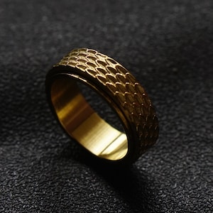 Peut inclure: Une bague dorée avec une surface texturée et un motif. La bague est en métal et a une finition lisse et polie.