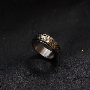 May include: A silver ring with a gold leaf design. The ring is a spinner ring, meaning the band spins freely.