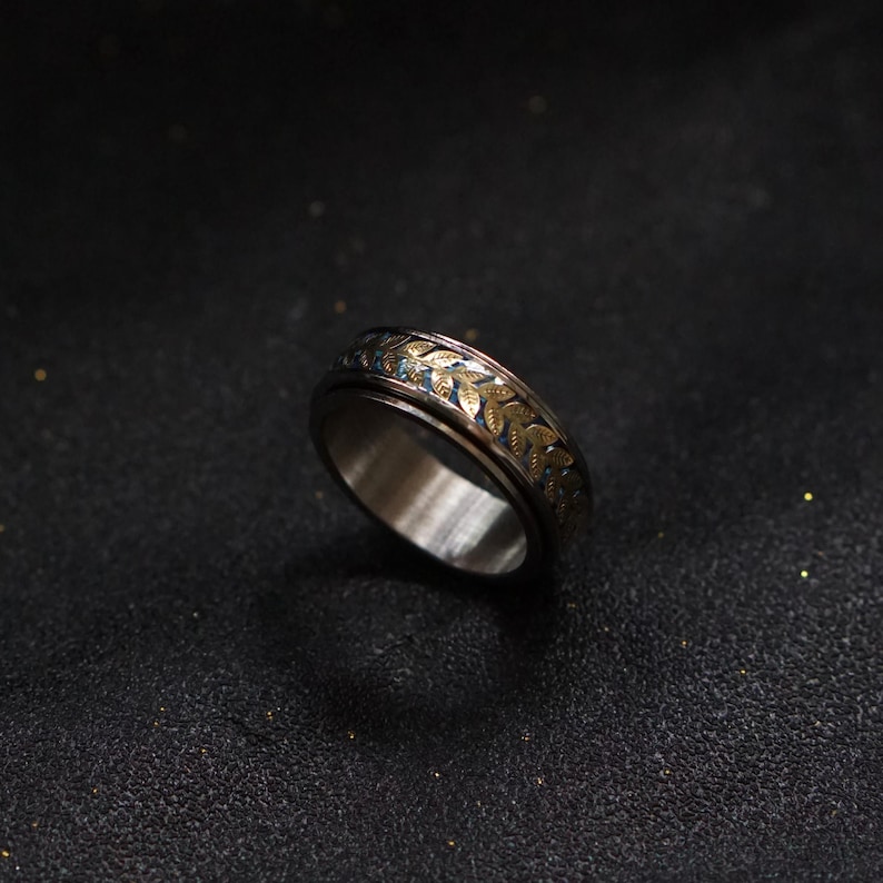 May include: A silver ring with a gold leaf design. The ring is a spinner ring, meaning the band spins freely.