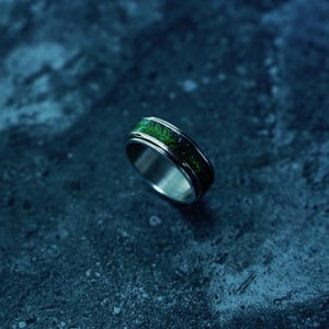May include: A silver ring with a green and black patterned band. The ring has a polished finish and a detailed design. The band features a vibrant green color with dark accents. The ring is a piece of jewelry.