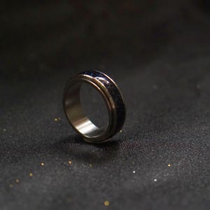 May include: A silver spinning ring with a blue and black inlay. The ring is on a black surface.
