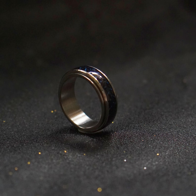 May include: A silver spinning ring with a blue and black inlay. The ring is on a black surface.