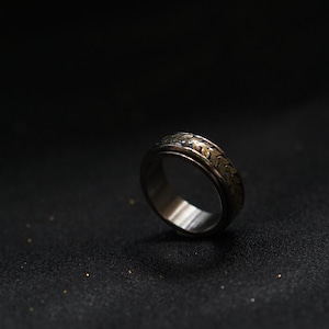May include: A silver ring with a gold and blue patterned band. The ring is on a black surface.