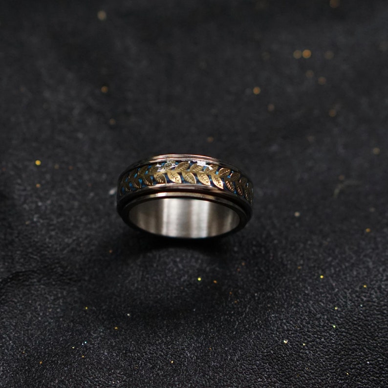 May include: A silver ring with a blue and gold band featuring a leaf design.
