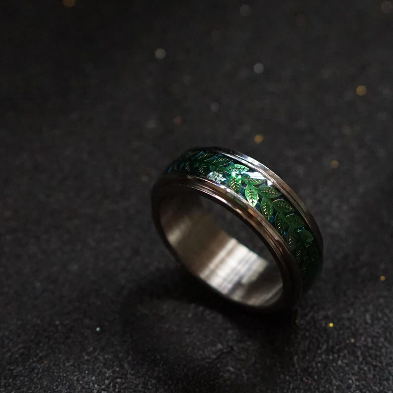 May include: A silver ring with a green leaf design. The ring is made of metal and has a polished finish.