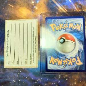 May include: A Pok&eacute;mon trading card in a protective sleeve next to a certificate of authenticity. The card features a red, white, and blue Pok&eacute; Ball design and the word "Pok&eacute;mon". The certificate has lines for title, artist, date, and info.