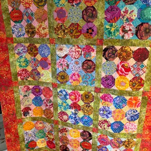 May include: A handmade quilt featuring a vibrant floral pattern. The quilt showcases colorful, circular flower designs in various hues, including red, pink, blue, and yellow, set against a green and red background. The quilt is a patchwork design.