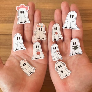 May include: A set of ten ghost stickers with various designs, including a ghost wearing a cowboy hat, a ghost with a flower crown, and a ghost holding a pumpkin. The stickers are white with black outlines and are perfect for adding a spooky touch to any project.