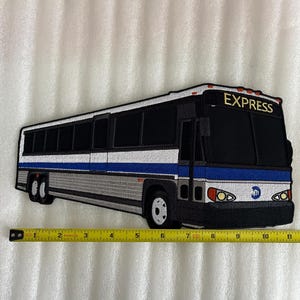 May include: A white and black embroidered patch of a New York City bus with the word "EXPRESS" on the front. The bus has a blue stripe and the MTA logo on the side. The patch is approximately 10 inches long.