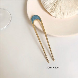 May include: A gold hair stick with a blue marble-like design at the top. The stick is 10 cm long and 2 cm wide.