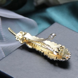 Peut inclure: Une barrette dor&eacute;e en forme de plume. La barrette pr&eacute;sente un design d&eacute;taill&eacute; avec de petits ornements scintillants. La barrette est en m&eacute;tal et poss&egrave;de un fermoir de type barrette.