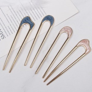 May include: Set of five gold hair sticks with decorative tops. Two sticks have blue tops with a swirl pattern, and three sticks have pink tops with a swirl pattern.