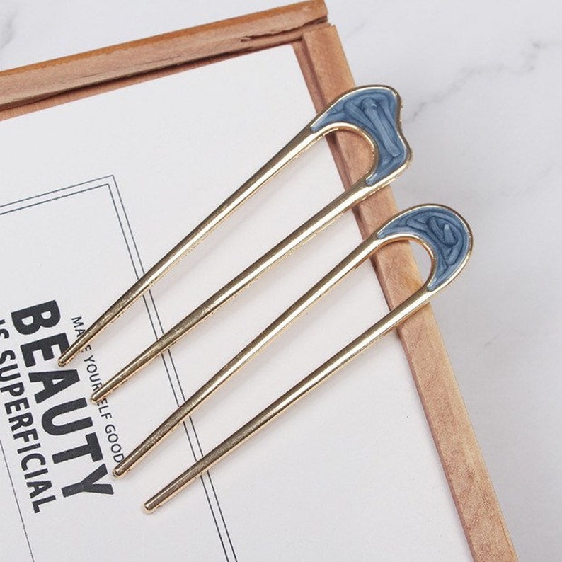 May include: Two gold hair sticks with blue enamel accents. The enamel has a marbled design. The sticks are about 10 inches long.