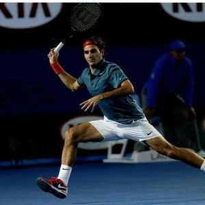 May include: A tennis player in a blue shirt and white shorts swings a tennis racket. The player is wearing a red headband and is in mid-swing. The player is on a blue tennis court.