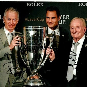 May include: Three men, including tennis player Roger Federer, holding a silver trophy with the inscription "Laver Cup" on it. The men are smiling and wearing suits. The background is black with the word "ROLEX" in white letters.