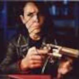 May include: A close-up of a person holding a silver revolver with a wooden handle. The person is wearing a black leather jacket and has a serious expression on their face.