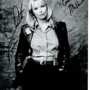 May include: Black and white photograph of a woman with blonde hair wearing a button-down shirt, black jacket, and black pants. The image includes two signatures and the text "Connie McDowell".