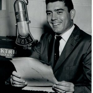 May include: Black and white photograph of a smiling man in a suit, holding papers near a microphone. The microphone has the letters "KTRH" on it. The signature "Dan Rather" is written above the man's head.