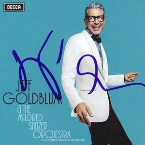 May include: A blue and white album cover with a photo of Jeff Goldblum in a white tuxedo jacket. The album title is "Jeff Goldblum & The Mildred Snitzer Orchestra" and the text "The Capitol Studios Sessions" is below the title. The album cover is signed in blue ink.