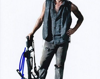 May include: A man wearing a black vest and jeans holds a crossbow. He has a small cut on his cheek. The crossbow is black and has a blue string.