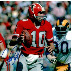 May include: A football player in a red jersey with the number 10 on it, wearing a white helmet with a red falcon logo, runs with the ball. He is being pursued by a player in a blue and white jersey with the number 80 on it.