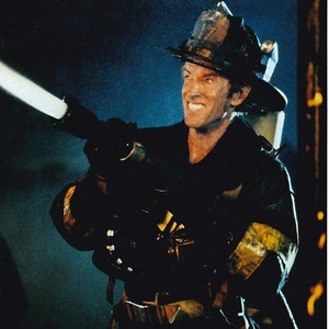 May include: A firefighter in a black uniform and helmet holds a fire hose with a white stream of water coming out of the nozzle.