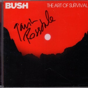 May include: A red CD case with a black silhouette of mountains and a white circle in the sky. The text "BUSH" and "THE ART OF SURVIVAL" are printed on the case. The case is signed "Tank  Rossdale".