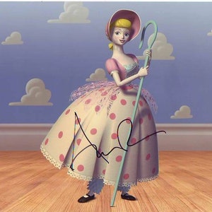 May include: A pink and white polka dot dress with a white lace trim and a blue shepherd's crook. The dress is worn by a doll with blonde hair and a pink hat. The doll is standing on a wooden floor with a blue and white cloud background.