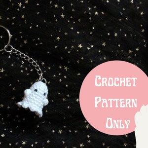 May include: White crocheted ghost keyring with a silver chain and ring. The ghost has two black eyes and a small smile. The background is black with gold glitter stars. The text "CROCHET PATTERN ONLY" is written in white on a pink circle.