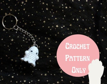 Puede incluir: Llavero de fantasma blanco tejido a crochet con una cadena y un anillo plateados. El fantasma tiene dos ojos negros y una pequeña sonrisa. El fondo es negro con estrellas doradas brillantes. El texto "CROCHET PATTERN ONLY" está escrito en blanco sobre un círculo rosa.