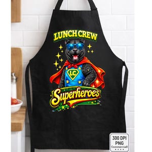 Puede incluir: Delantal negro con un dibujo de pantera de dibujos animados con gafas de sol y una capa de superh&eacute;roe. El texto "LUNCH CREW Superheroes" se muestra en amarillo y verde. La pantera tiene un logotipo LC azul y amarillo.