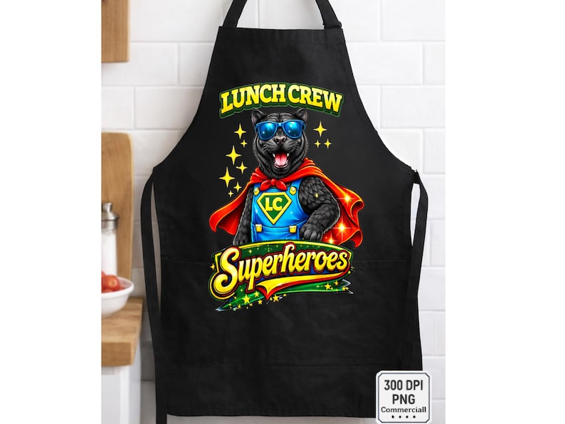 Puede incluir: Delantal negro con un dibujo de pantera de dibujos animados con gafas de sol y una capa de superh&eacute;roe. El texto "LUNCH CREW Superheroes" se muestra en amarillo y verde. La pantera tiene un logotipo LC azul y amarillo.