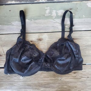 May include: Black bra with adjustable straps. The bra features a satin-like finish with lace detailing on the cups. The underwire bra has a classic design with a hook-and-eye closure at the back. The bra is designed for support and comfort.